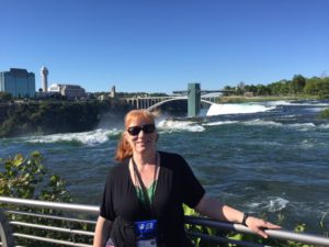 Rhonda stands at at a rail with Niagara Falls in the background.