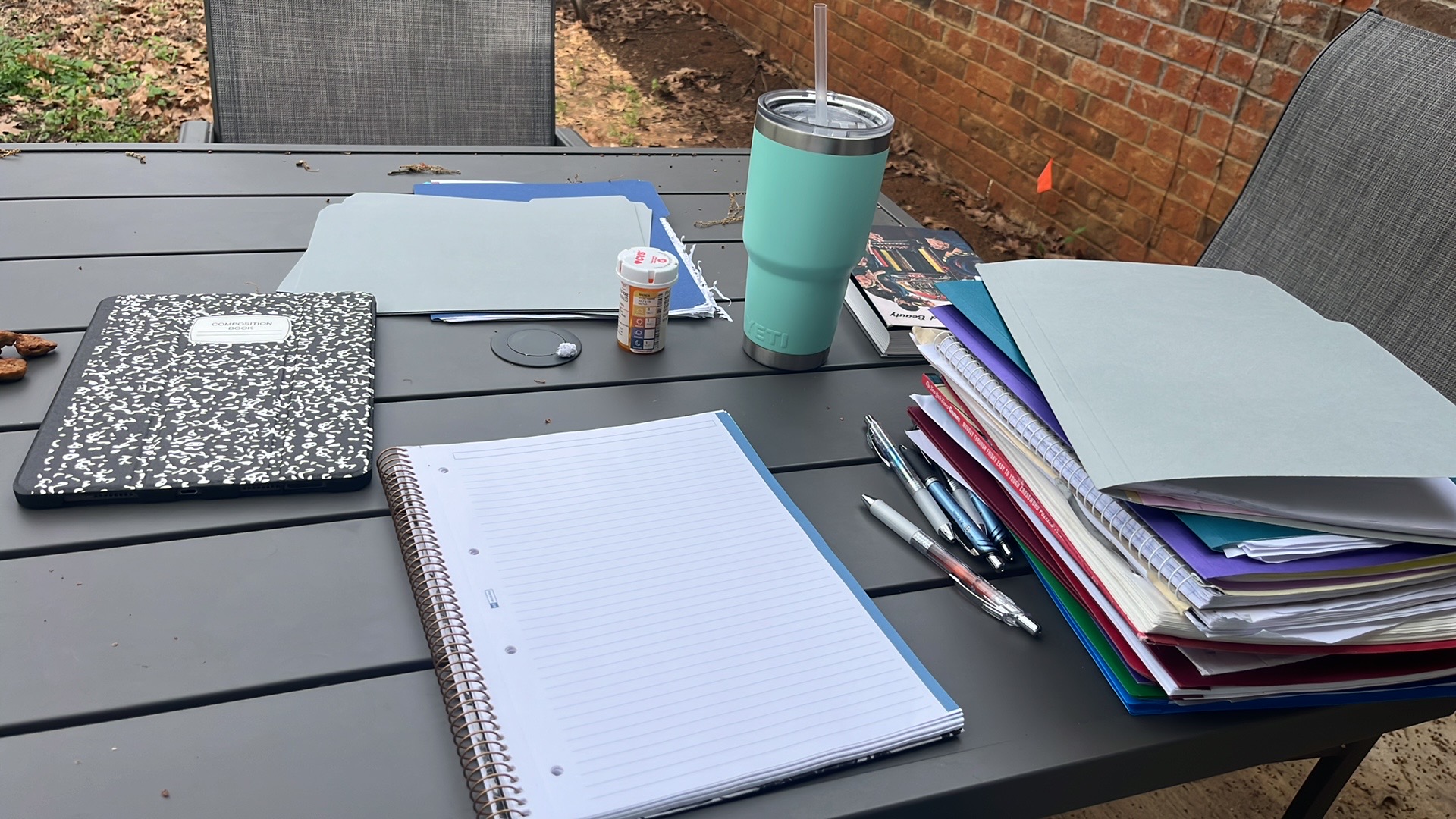 Outdoor table with notebooks, an insulated tumber, and pens