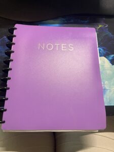 Purple notebook cover that says notes with black discs.