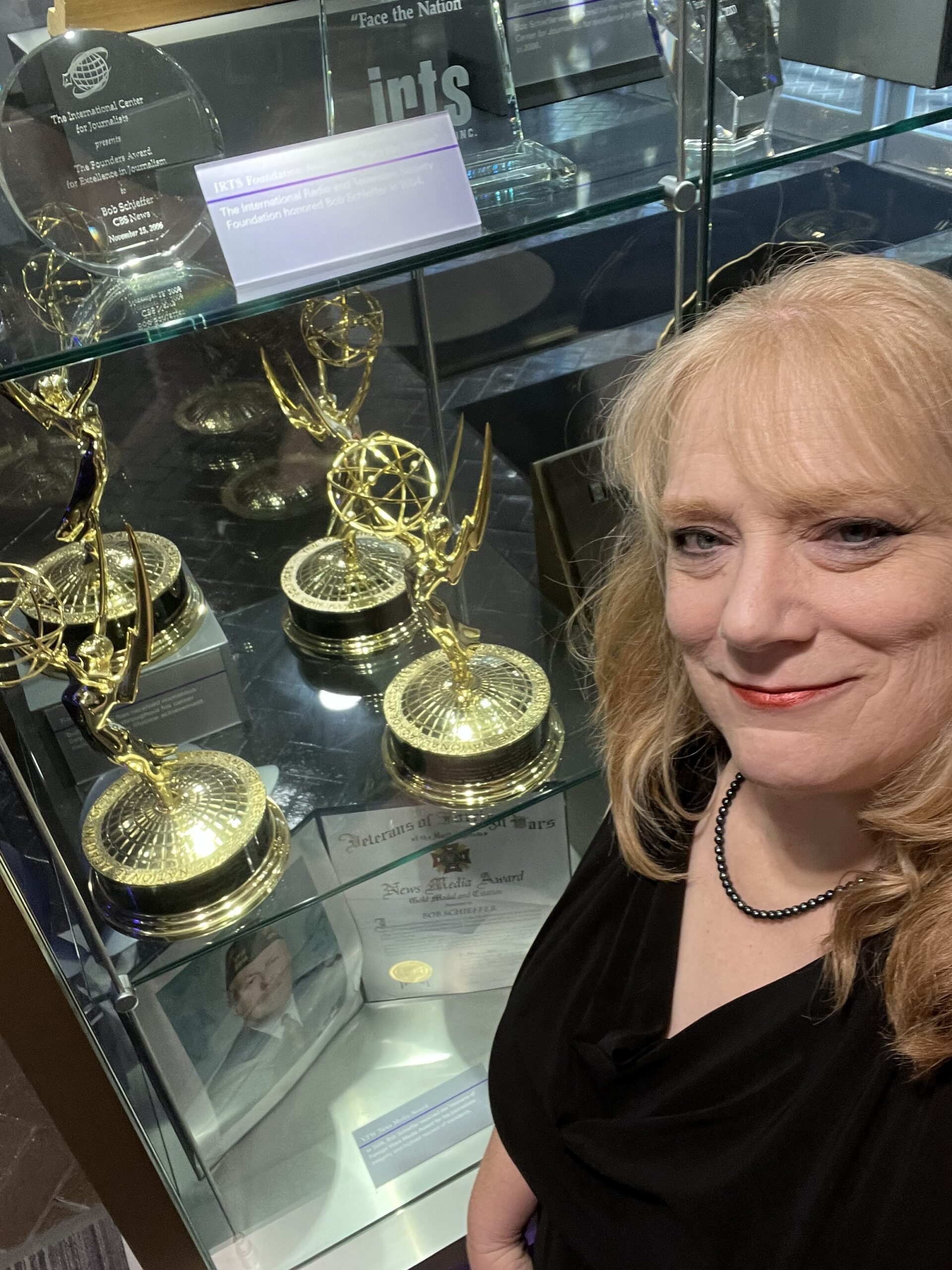 Rhonda standing in front of Emmy Awards and other awards in a glass case.