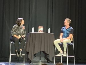 Neil Patrick Harris on stage sitting at a table with an interviewer.